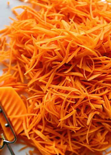 Shredded carrots piled together, with a peeler in the corner.