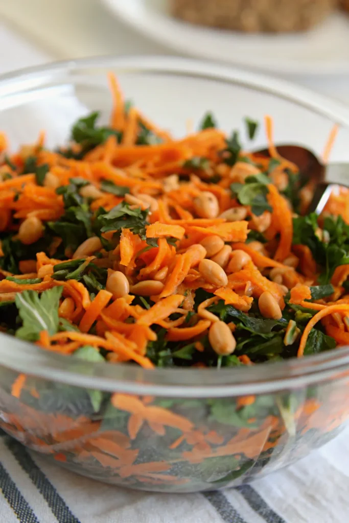 Shredded carrots, parsley, and chickpeas in a glass salad bowl.