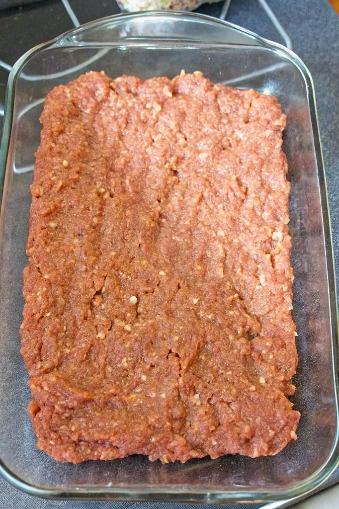 Meatloaf mixture spread evenly in a glass baking dish, ready to be baked.