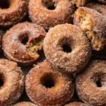 : A close-up of cinnamon sugar-coated apple cider donuts with one donut cut in half, revealing its soft, spongy interior.