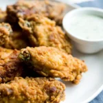 A plate of crispy fried chicken wings with a bowl of ranch dipping sauce on the side.